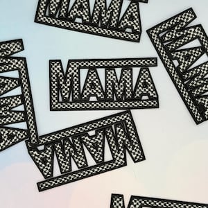Puede incluir: Parches bordados con la palabra "MAMA" en un estilo de letras en bloque audaz. Los parches presentan un patrón de cuadros blancos y negros dentro de las letras y un borde negro. Varios parches están dispersos sobre un fondo claro.