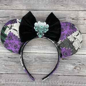 May include: Purple and black Haunted Mansion Mickey Mouse ears with a black velvet bow and a green and white Haunted Mansion logo charm.