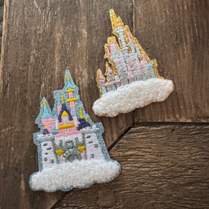 May include: Two embroidered iron-on patches featuring a pink and blue castle with white clouds. The castles are surrounded by white fluffy clouds.