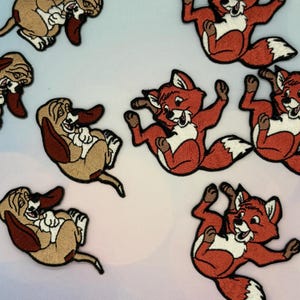 May include: Embroidered patches featuring cartoon foxes in shades of red, white, and brown, and cartoon dogs in shades of tan, brown, and white. The patches are designed with detailed stitching and are likely for clothing or accessories.