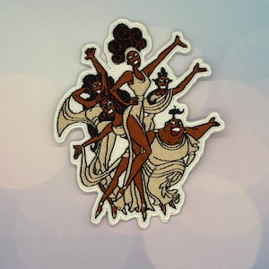 Könnte beinhalten: Gestickter Aufnäher mit fünf Frauen in cremefarbenen Kleidern mit brauner Haut und dunkelbraunem Haar. Der Aufnäher hat einen weißen Rand und ist vor einem hellblauen und violetten Hintergrund platziert. Die Frauen befinden sich in einer Tanzpose.