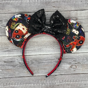 May include: Black and red mouse ears with a black sequin bow. The ears feature a graphic print of Deadpool with a unicorn and other cartoon characters.