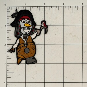 May include: Embroidered patch featuring a cartoon pirate snowman character. The patch has a black hat, red bandana, and a brown vest. The snowman is holding a small red bird. The patch is approximately 2 inches tall.