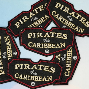 May include: Black and red embroidered patches with the text "PIRATES of the CARIBBEAN" in a vintage font. The patches have a decorative border and a small emblem. Several patches are visible.