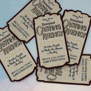 May include: Several embroidered patches with a vintage design. Each patch features the text "Disneyland Casting Agency" in a serif font, along with a quote and the name Walter Elias Disney. The patches have a cream background with burgundy borders.