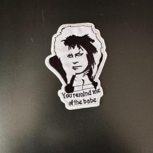 May include: White embroidered patch with a black and white image of a person with long hair and the text "You remind me of the babe".