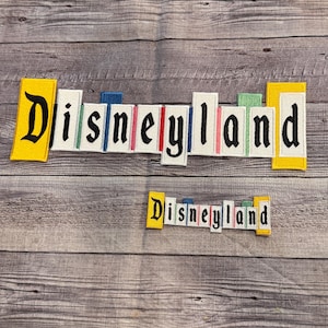 May include: Two embroidered patches with the text "Disneyland" in black letters on a white background. The larger patch has individual letters with colorful borders. The smaller patch has the letters together with a yellow border.