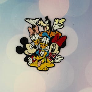 Puede incluir: Un parche bordado colorido que presenta un grupo de personajes de dibujos animados clásicos, incluidos Mickey Mouse, Minnie Mouse, el Pato Donald, Daisy, Goofy y Pluto, todos dispuestos juntos en un grupo apretado con contornos negros.