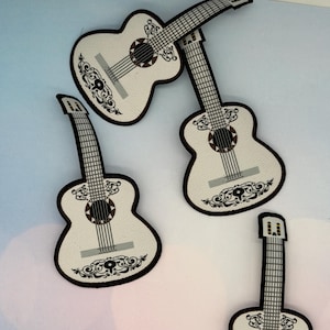 May include: White guitar-shaped patches with brown trim and decorative black scrollwork. The patches feature a sound hole and strings, resembling a traditional acoustic guitar. The patches are ideal for sewing onto clothing or accessories.