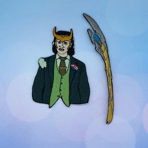 May include: Embroidered patch set featuring a character in a green suit with a gold horned helmet and a staff. The character has a green vest, a tie, and a pin. The staff is silver and gold.