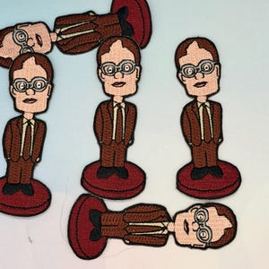 May include: Embroidered patches featuring a cartoon character in a brown suit, glasses, and a red base. The patches are in various orientations, showcasing the character's face and attire. The patches are likely for clothing or accessories.