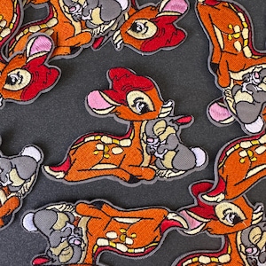 以下が含まれることがあります： ディズニーのキャラクター、バンビと友達のトンパの刺繍パッチ。 パッチは主にオレンジ、赤、グレー、ピンクで、詳細なステッチが施されています。 パッチはグレーのボーダーでデザインされています。