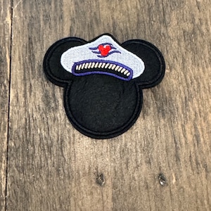 May include: A black felt Mickey Mouse head with a white captain's hat with a red heart and blue waves. The hat has a gold band with a white stripe.