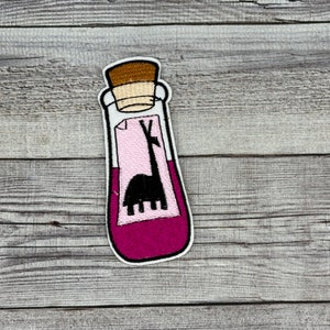 May include: A pink and white glass bottle with a cork stopper. The bottle contains a pink liquid and a black silhouette of a llama on a white label.