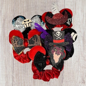 Puede incluir: Una colección de seis scrunchies para el cabello con temática de Disney con varios personajes, incluyendo un pirata, una calavera y una bruja. Los scrunchies están hechos de terciopelo rojo, negro y morado con adornos de purpurina y lentejuelas.
