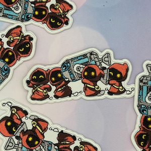 May include: Embroidered patch featuring four small figures in hooded orange robes with glowing yellow eyes, carrying a large grey and blue mechanical device. The design has a white border and depicts the characters in a cartoon style.
