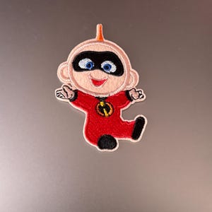 Può includere: Toppa ricamata da stirare con un bambino dei cartoni animati in un costume da supereroe rosso e nero. Il bambino ha una maschera nera e un simbolo rosso sul petto.