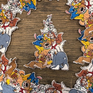 May include: Embroidered patches featuring various cartoon dog characters, including Stitch, arranged in a circular pattern. The patches are colorful with detailed stitching, set against a wooden background.