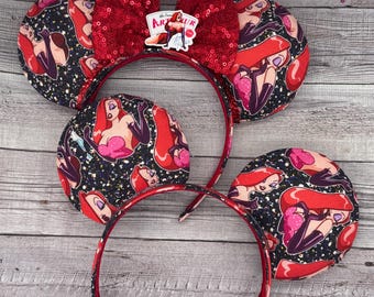 May include: Red and black mouse ears with a red sequin bow and a cartoon character print. The character is a woman with red hair and a red dress. The text on the bow says "The Toon's"