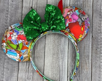 Op de afbeelding: Groen glitterende strik hoofdband met een kleurrijk stoffen ontwerp met personages uit de film Robin Hood. Het stoffen ontwerp bevat Robin Hood, Little John, Maid Marian en Prins John.