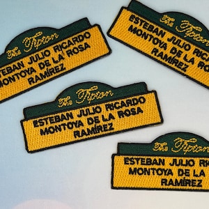 Puede incluir: Parches bordados con el texto "The Tipton" y el nombre "ESTEBAN JULIO RICARDO MONTOYA DE LA ROSA RAMIREZ" en hilo amarillo sobre un fondo verde y dorado. Los parches son rectangulares con la parte superior curvada.
