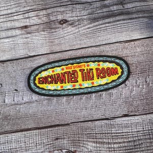 May include: A black and yellow embroidered patch with the text "Walt Disney's Enchanted Tiki Room" in red and white lettering.