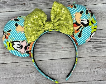 May include: A pair of green and blue Minnie Mouse ears with a green sequin bow. The ears feature a cartoon image of Goofy.