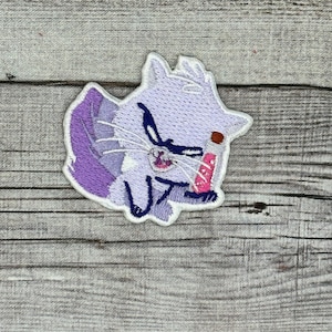May include: Purple and white embroidered iron-on patch of a cartoon cat with an angry expression.