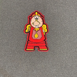 May include: Red and yellow embroidered patch of a cartoon clock character with a crown and a large gold key.