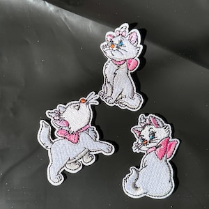 May include: Three embroidered patches featuring a white cat with a pink bow and a pink bow on its head. The cat patches are in different poses, with one sitting, one looking up, and one sitting.