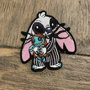 Könnte beinhalten: Gestickter Aufnäher mit einer Mischung aus Charakteren. Das Design kombiniert Stitch aus Lilo & Stitch mit Jack Skellington aus The Nightmare Before Christmas, der Sally hält. Der Aufnäher hat ein Farbschema aus Schwarz, Weiß, Rosa, Blau und Orange.