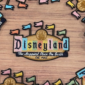 May include: An embroidered patch featuring the Disneyland logo with the text "Disneyland" in colorful letters and the tagline "The Happiest Place On Earth" with the year "Est. 1955".