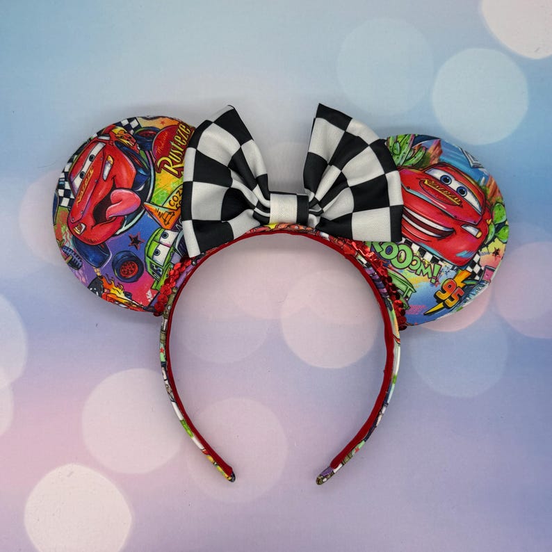 May include: A pair of mouse ears featuring a black and white checkered bow and ear designs with images of the Disney Cars movie characters. The headband is red with a patterned design on the inside.