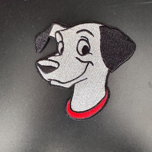 May include: Embroidered patch of a cartoon Dalmatian dog with black ears and a red collar. The dog is looking to the right and has a happy expression.