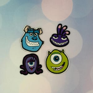 May include: Four embroidered patches featuring cartoon monster characters. One is a large blue furry creature with horns, one is a round green one-eyed monster, one is a small purple creature with three head spikes, and one is a purple oval-shaped monster.