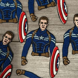 May include: Embroidered patches featuring Captain America in a blue and brown uniform, holding a red, white, and blue shield. The patches are detailed with facial features and uniform accents, ideal for clothing or accessories.