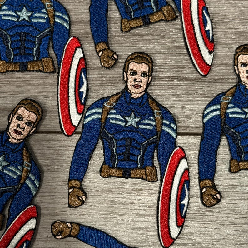 May include: Embroidered patches featuring Captain America in a blue and brown uniform, holding a red, white, and blue shield. The patches are detailed with facial features and uniform accents, ideal for clothing or accessories.