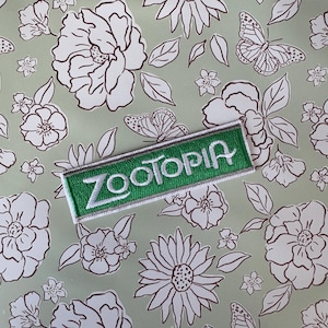 Puede incluir: Parche bordado verde y blanco con la palabra "Zootopia" en letras blancas.