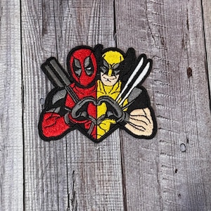 Może przedstawiać: Naszywka haftowana przedstawiająca Deadpoola i Wolverina w kształcie serca. Deadpool jest czerwony i czarny z maską, a Wolverine jest żółty i czarny z pazurami.