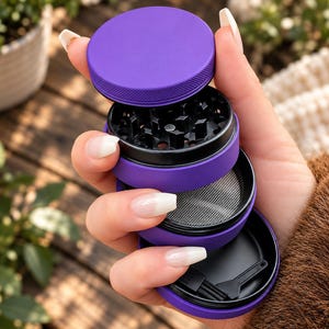 May include: A four-piece purple herb grinder with a matte finish. The device features a textured lid, a black interior grinding chamber with sharp teeth, a fine metal mesh screen for sifting, and a bottom storage compartment containing a small brush.