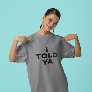Puede incluir: Una camiseta gris con el texto "I TOLD YA" impreso en negro.
