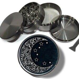 May include: A silver metal grinder with a black and white moon and stars design. The grinder has four parts and a small scraper tool.