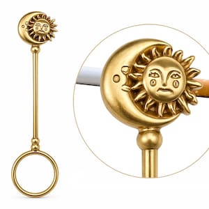 May include: A gold-colored cigarette holder featuring a sun and moon design. The holder has a ring for the finger and a long stem. The sun and moon are detailed with facial features. The holder is designed to hold a cigarette.