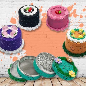 Pode incluir: Quatro moinhos de ervas em forma de bolo coloridos com um moinho verde com flores brancas e folhas verdes. Os moinhos são de metal e têm uma superfície texturizada.