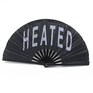 以下が含まれることがあります： 白い「HEATED」の文字が書かれた黒い折りたたみ式の扇子。扇子は黒い柄が付いており、小さな白い点で飾られています。