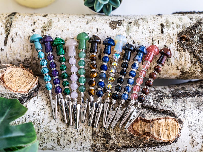 May include: A set of 12 colorful beaded hair clips with mushroom-shaped tops. Each clip features a different gemstone, including amethyst, malachite, rose quartz, aventurine, tiger's eye, lapis lazuli, clear quartz, sodalite, rose quartz, red jasper, and tiger's eye.