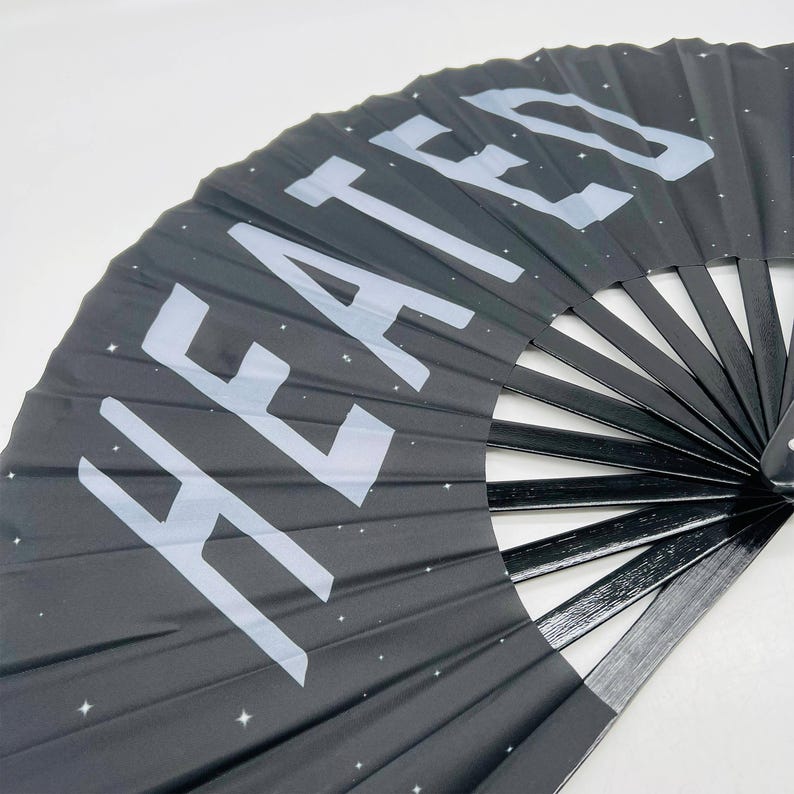 以下が含まれることがあります： 白い星の模様と「HEATED」という文字が前面に印刷された黒い折りたたみ式扇子