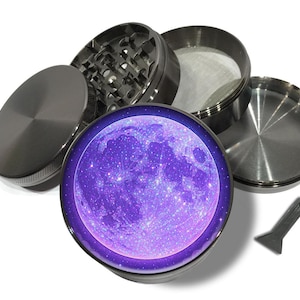 May include: A disassembled, silver-colored herb grinder with a purple and blue moon design on the top. The grinder is made of metal and includes a screen and a small scraper tool.