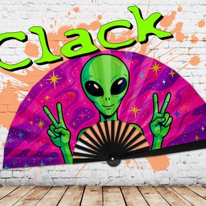 May include: A folding fan featuring a green alien with large black eyes, making a peace sign with both hands. The fan has a black handle and a vibrant design of pink, purple, and blue swirls with stars. The word "CLACK" is written in large, green letters above the fan.