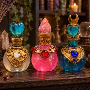 May include: Three decorative glass potion bottles with ornate gold-tone metal accents. The left bottle has a heart-shaped blue stopper, the center has a pink crystal stopper, and the right has a crescent moon and heart-shaped blue stopper.